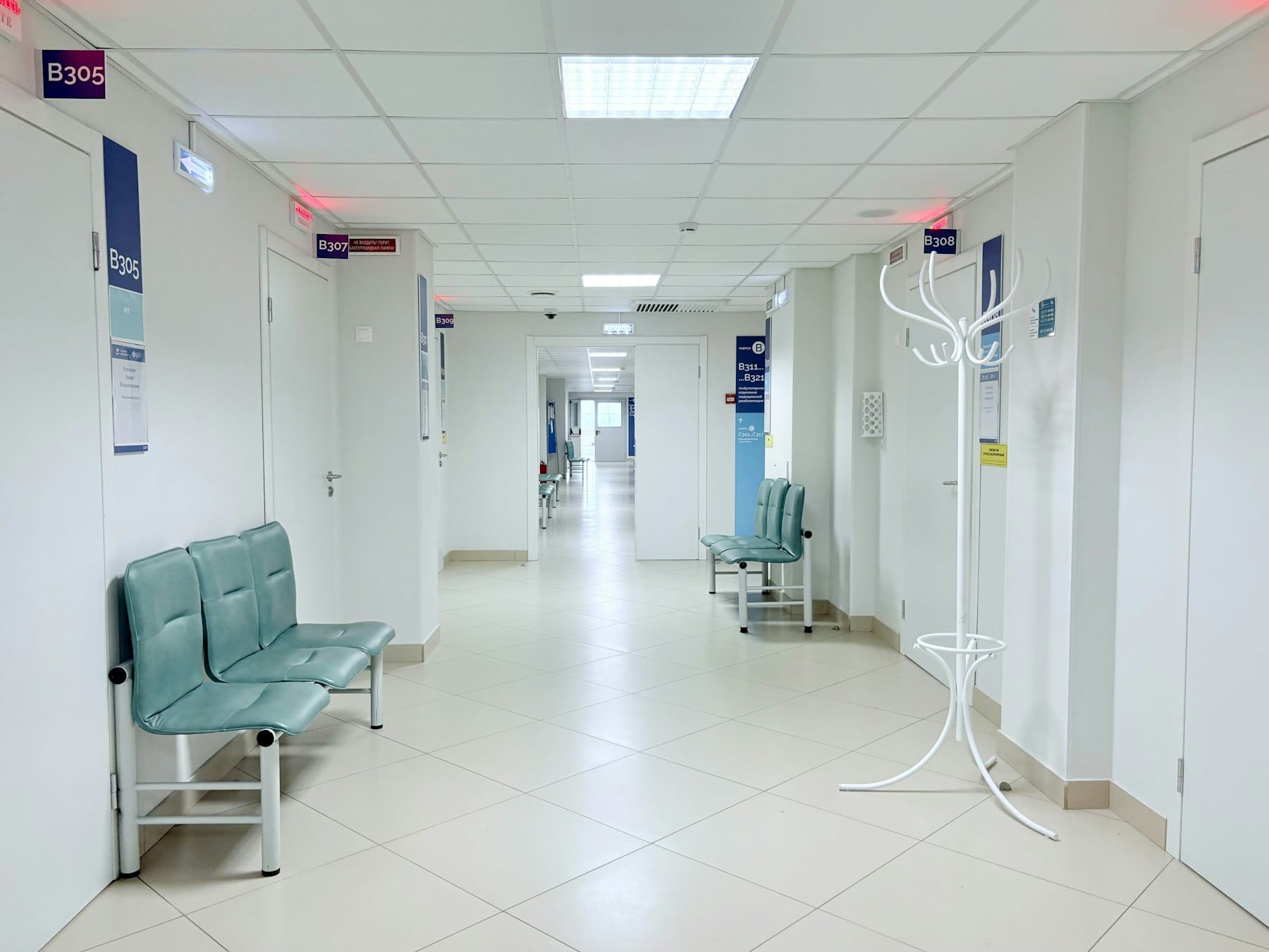 An empty hospital corridor with benches along the wall and closed doors