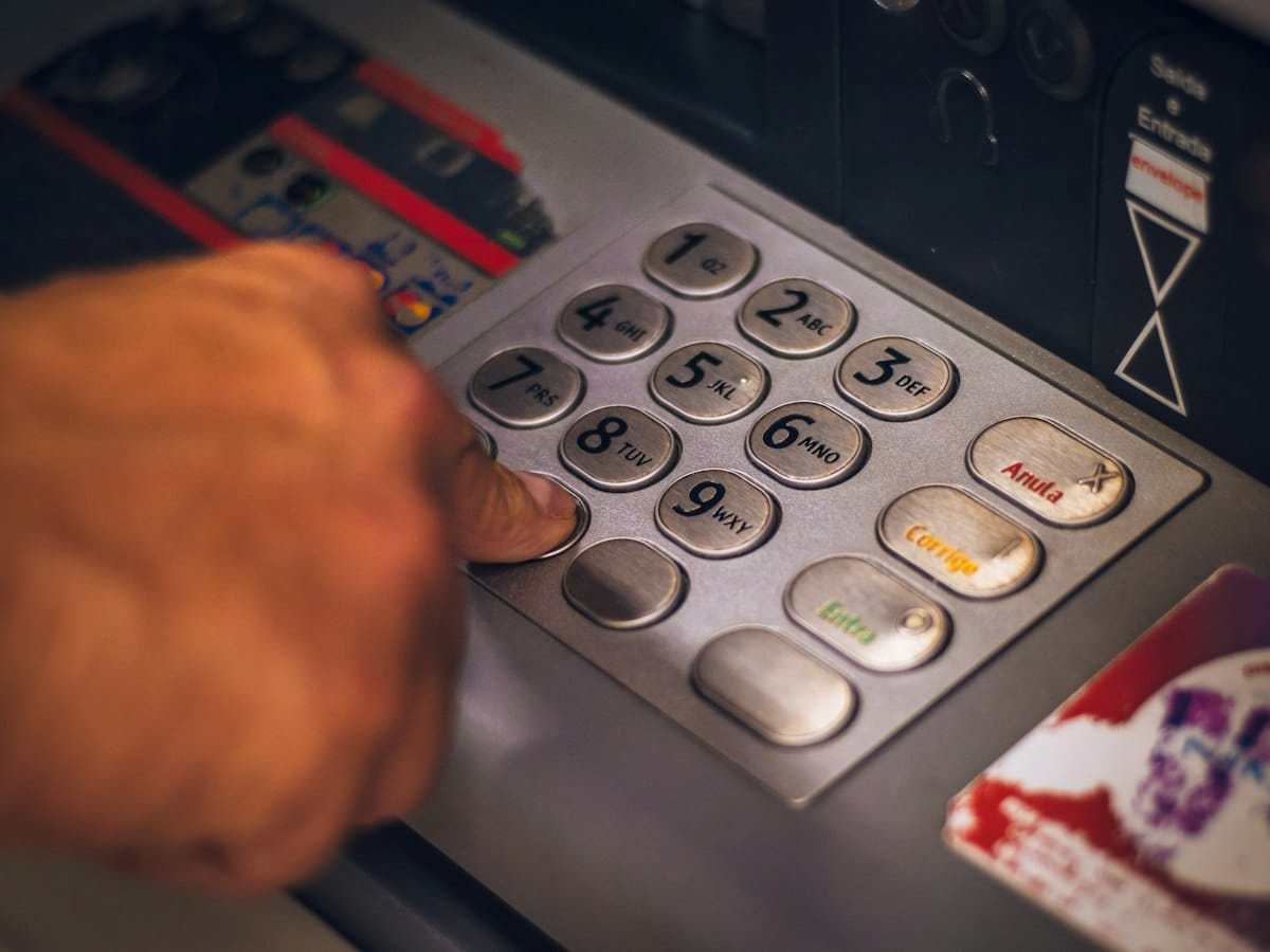 A finger pressing the metal keypad of a cash machine