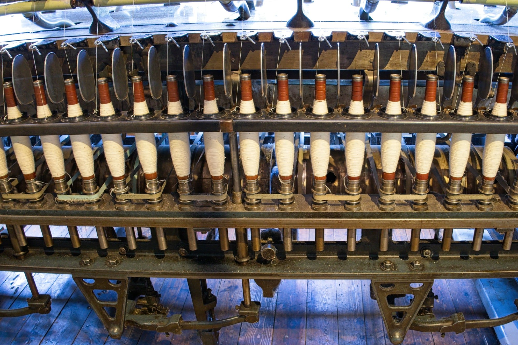 A row of white bobbins on an old spinning machine in a textile mill