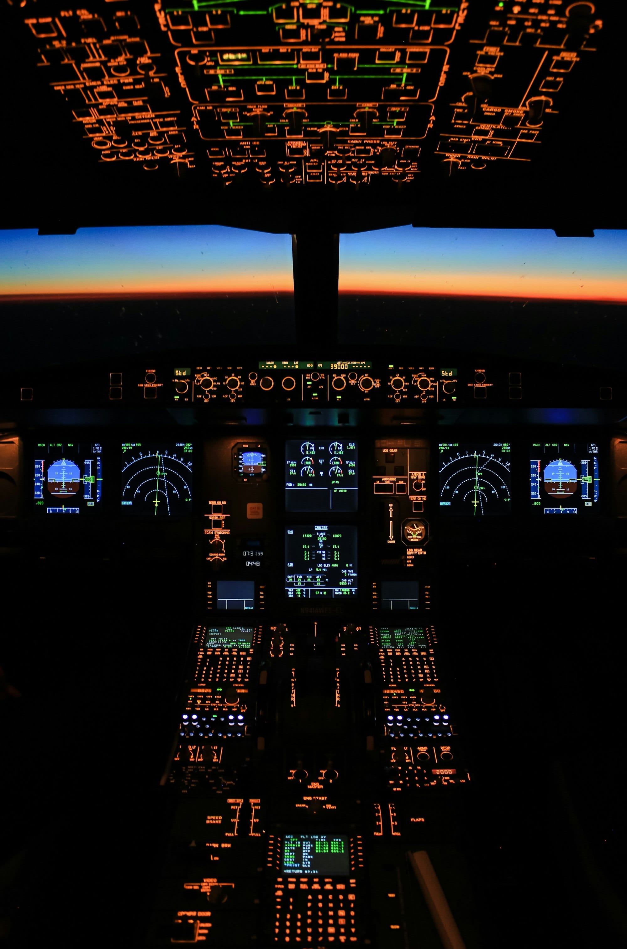 An airliner cockpit at night with glowing instrument panels and the horizon beyond the windows