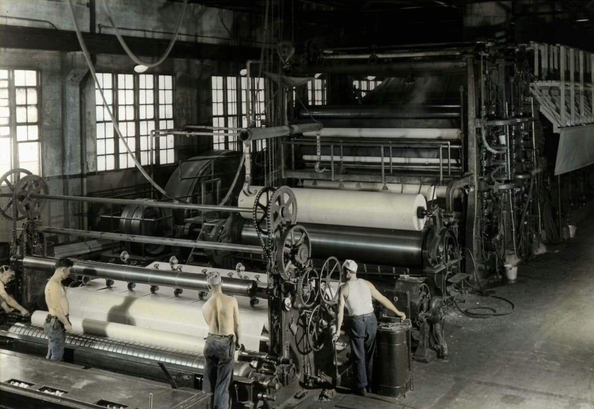 Archive photograph of workers operating large machinery in an early twentieth century paper mill