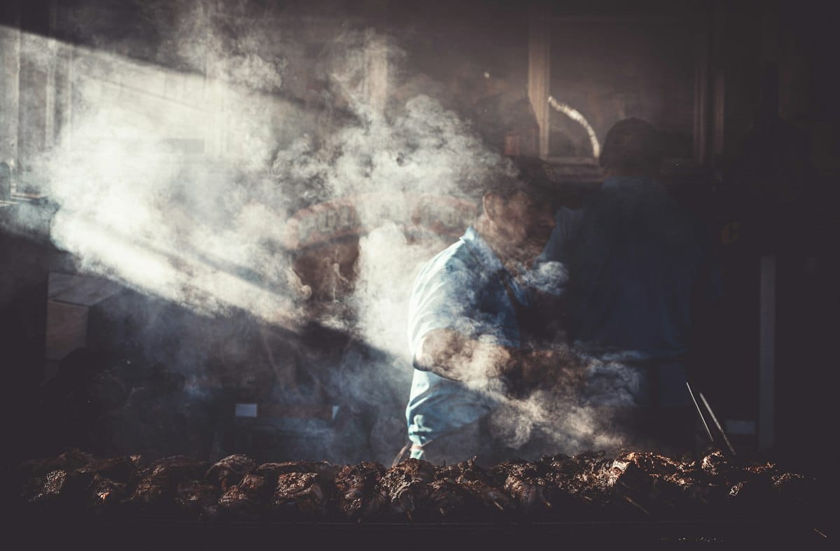 A man standing at an outdoor grill almost hidden by thick white smoke
