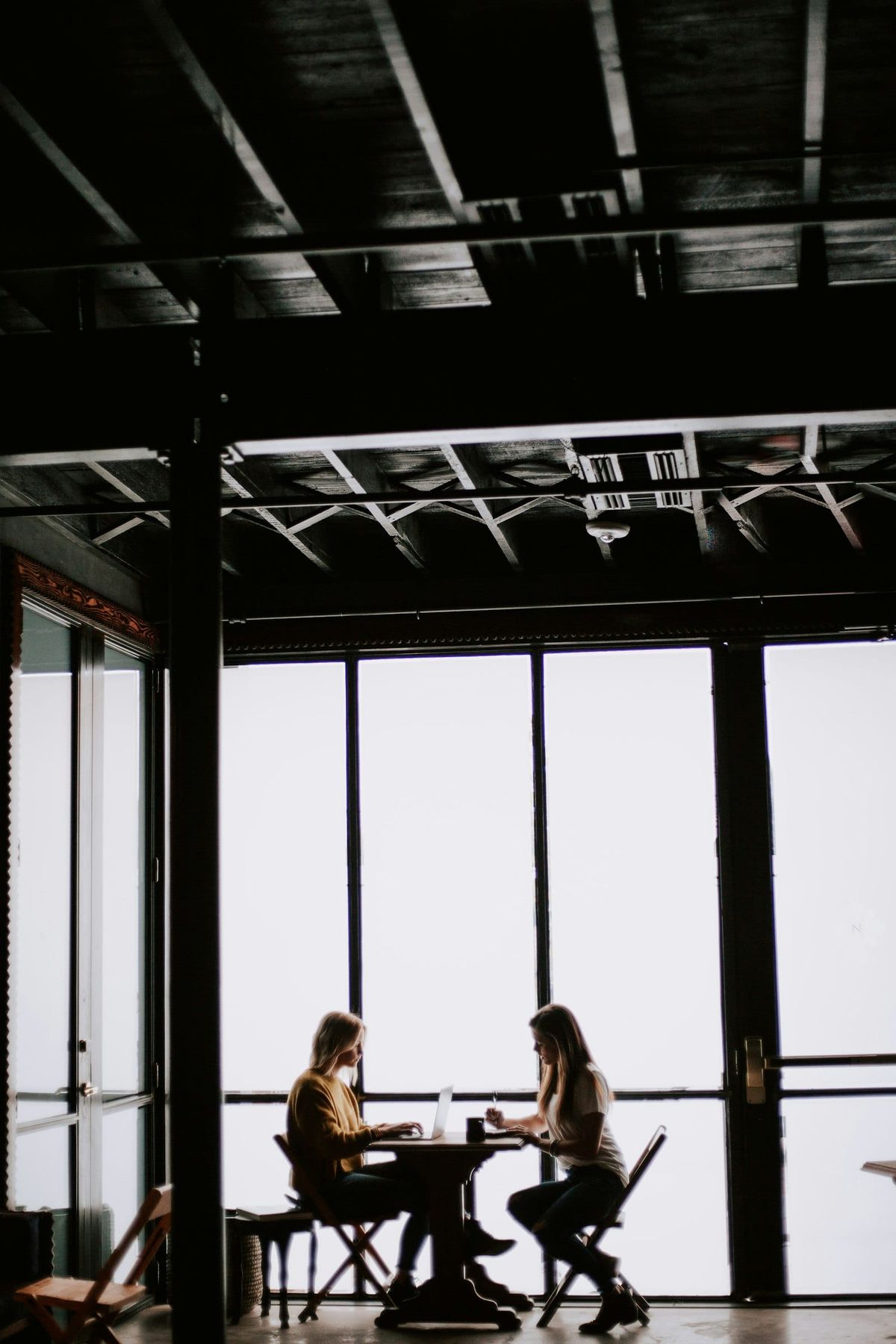 Two people sitting facing each other at a small table in a large empty room