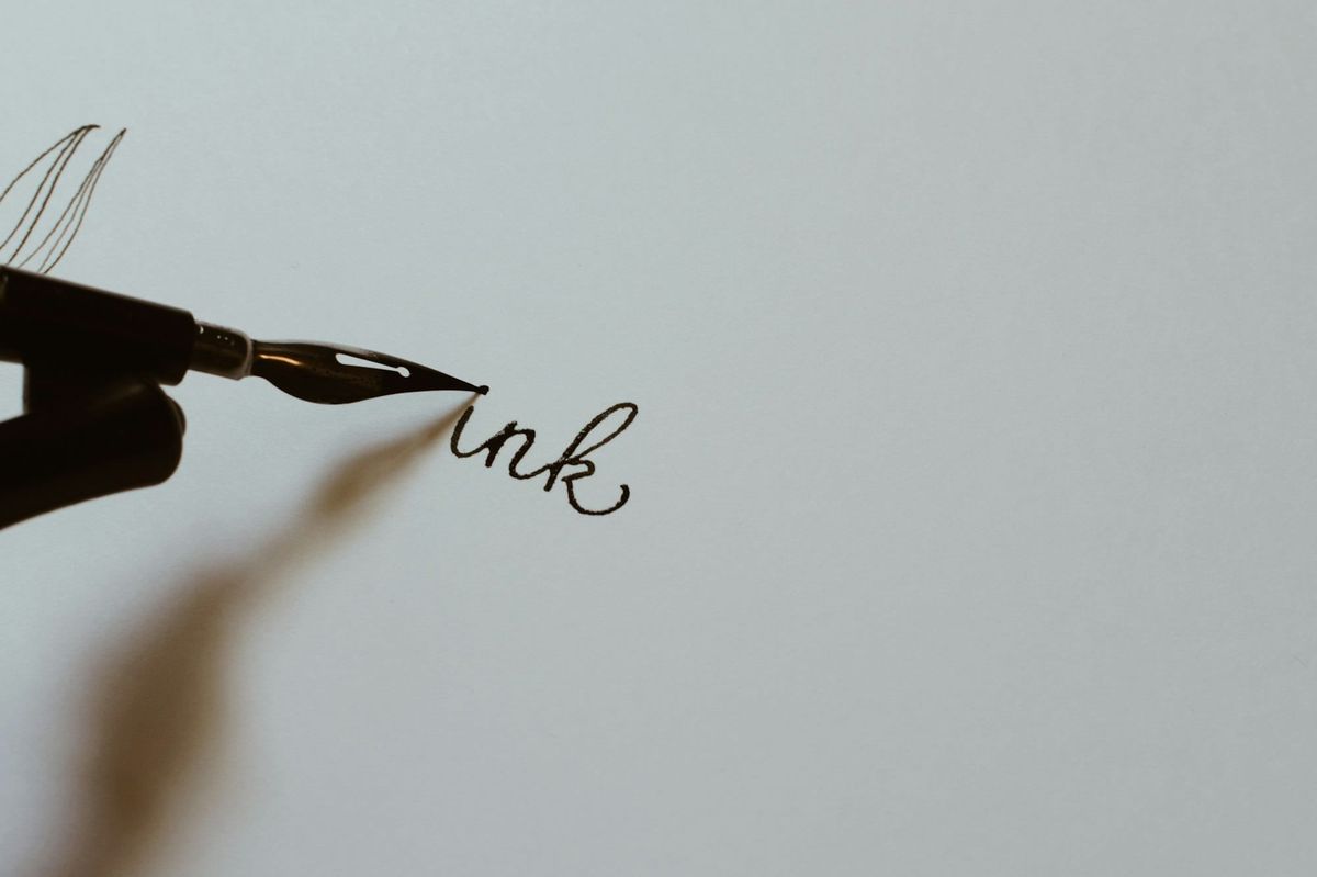 Close up of a hand writing in ink with a black fountain pen on white paper