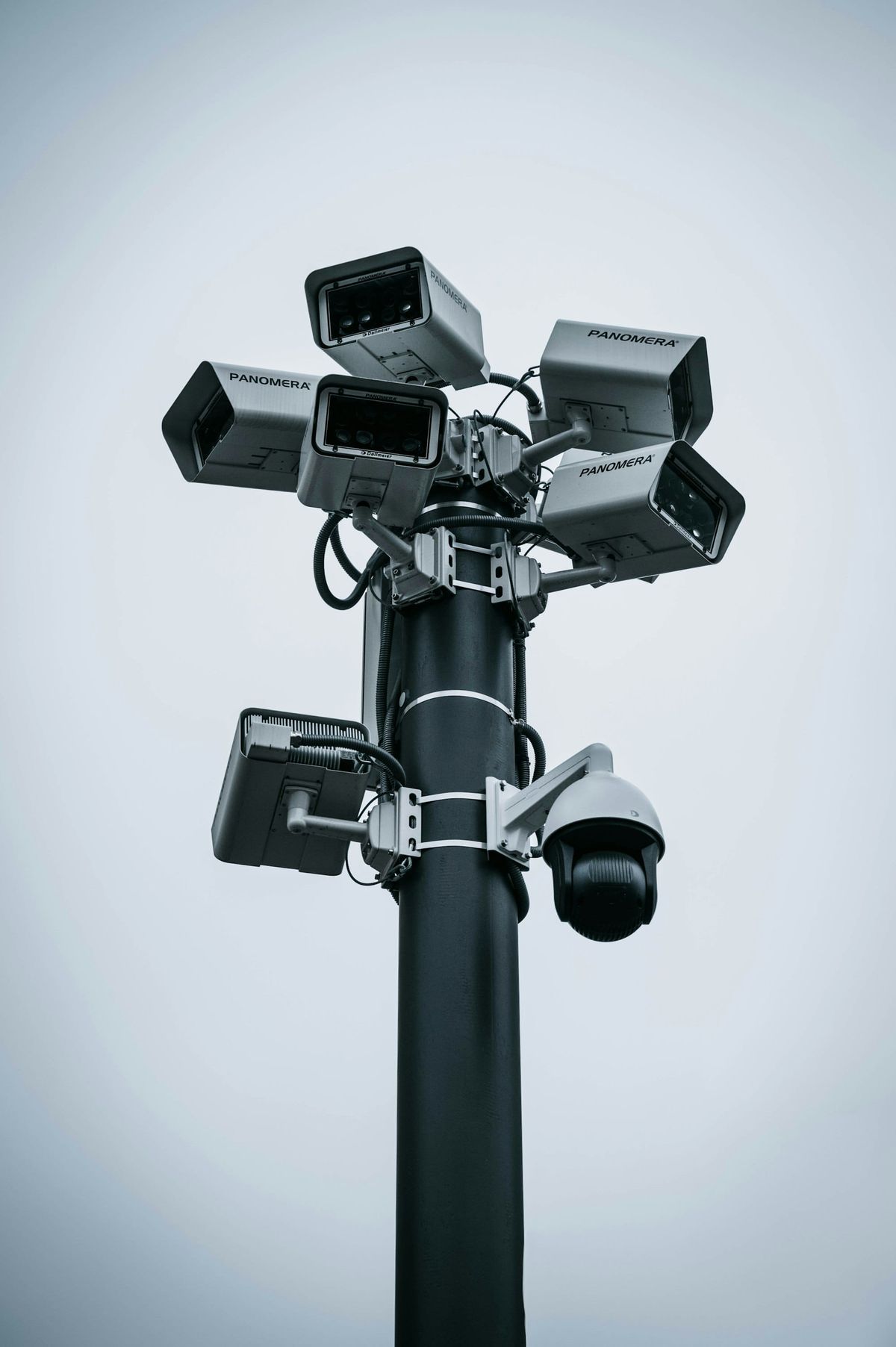 Several surveillance cameras mounted on a tall metal pole against the sky