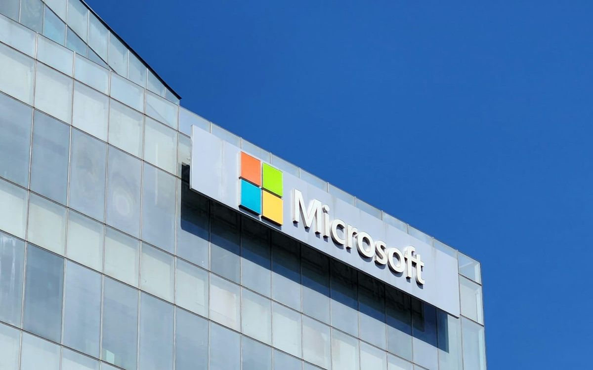 The Microsoft logo and wordmark on the glass side of an office building against a blue sky
