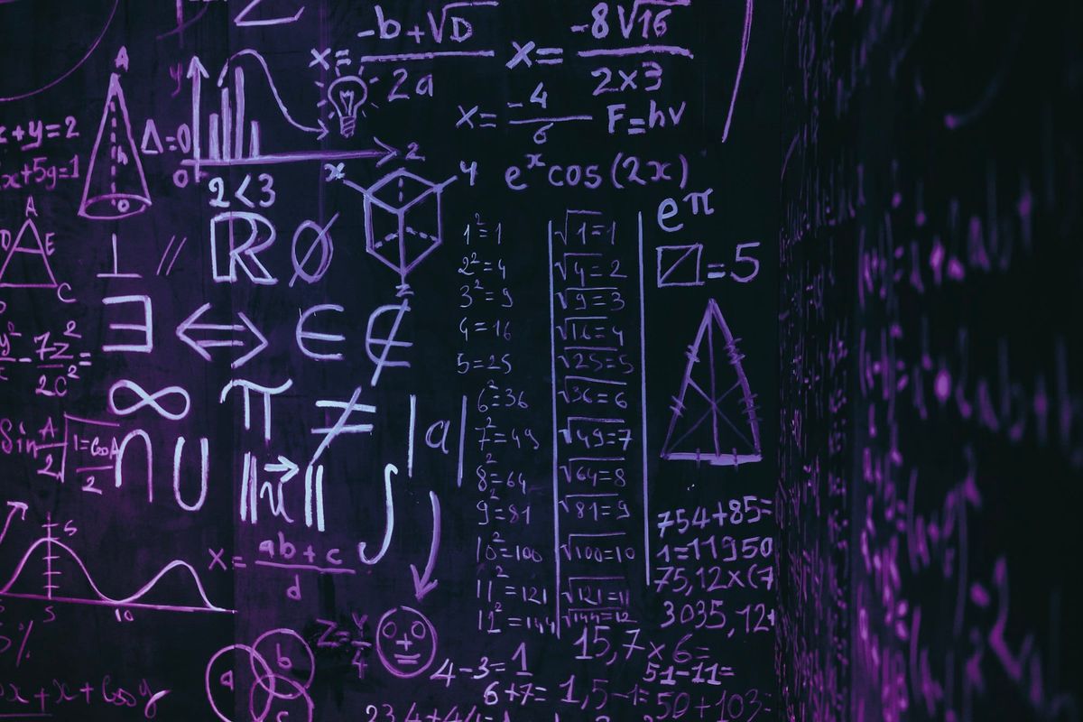 A dark blackboard covered in chalk equations, symbols and small graphs, lit in purple