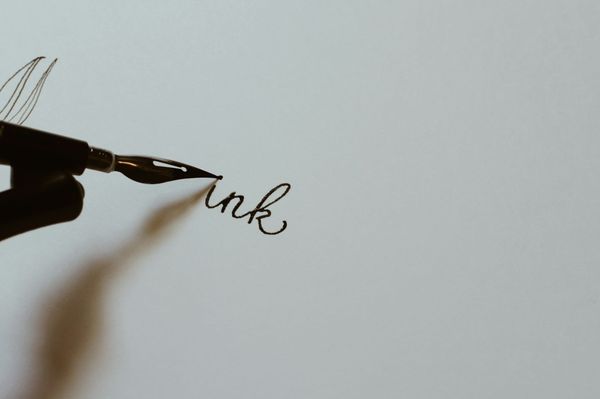 Close up of a hand writing in ink with a black fountain pen on white paper