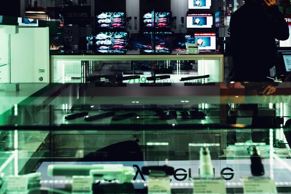 A glass display counter in an electronics shop, lit from inside, with a person standing behind it