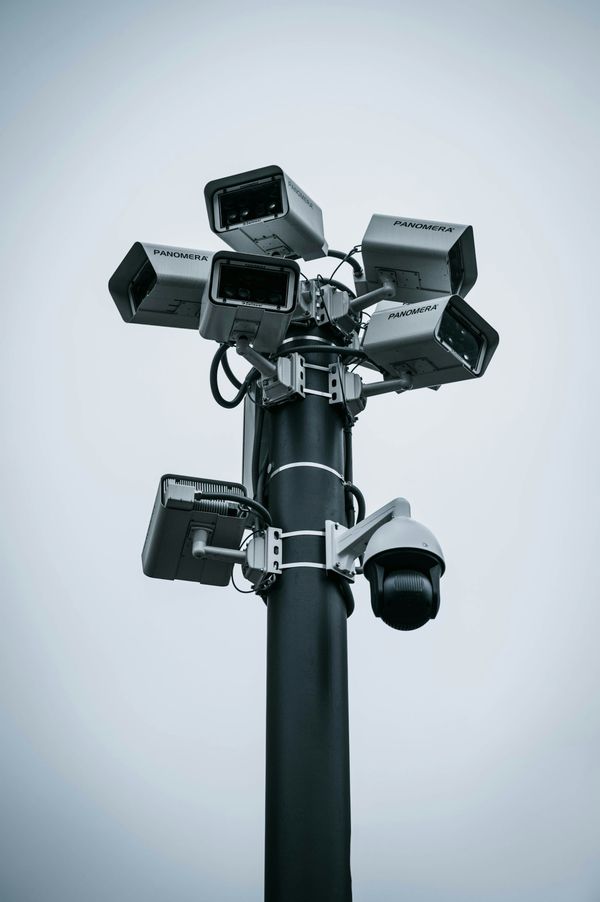 Several surveillance cameras mounted on a tall metal pole against the sky