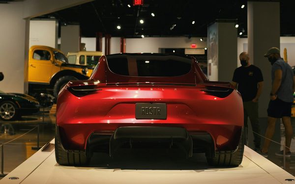 The red second-generation Tesla Roadster prototype from 2017, seen from behind on a display plinth in a car museum, with visitors nearby