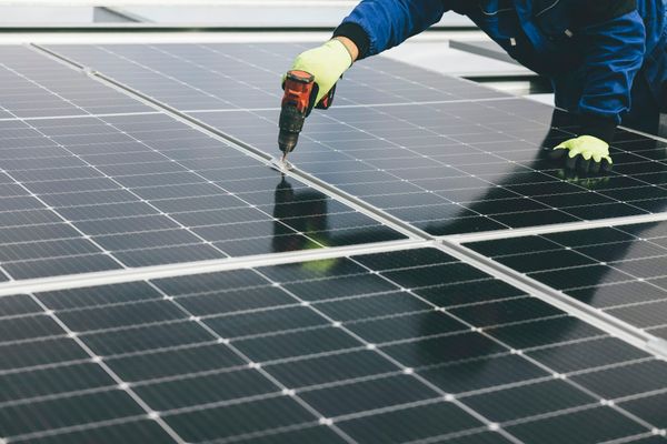 A technician in work clothes kneels over rows of solar panels, working on one of them