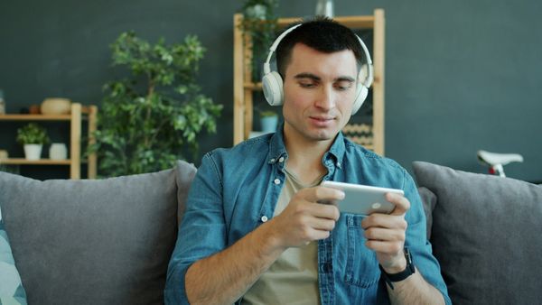 A man wearing headphones plays a game on a smartphone