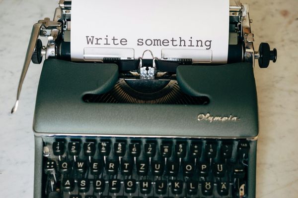 An Olympia typewriter on a marble surface with a sheet of paper reading Write something