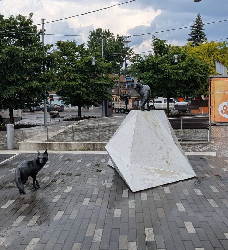 photo: trapezoidal monument with a pair of black fox statues on a brick plaza after a rain
