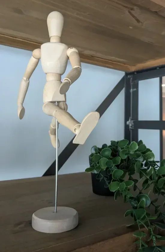 photo: wooden humanoid figure in dynamic mid-stride position on stand w/ plant adjacent