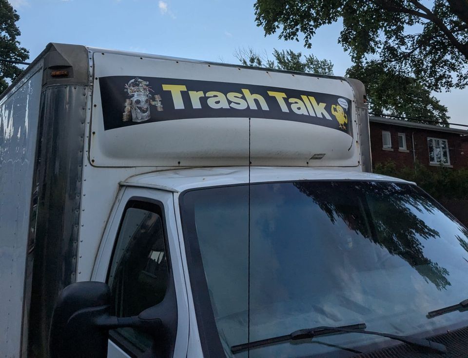 photo: banner on a truck: Trash Talk, featuring an anthropomorphic robot made of garbage and a canary with biceps