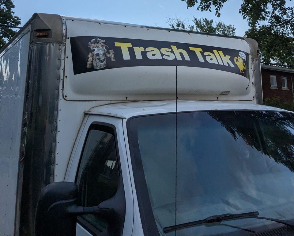 photo: banner on a truck: Trash Talk, featuring an anthropomorphic robot made of garbage and a canary with biceps