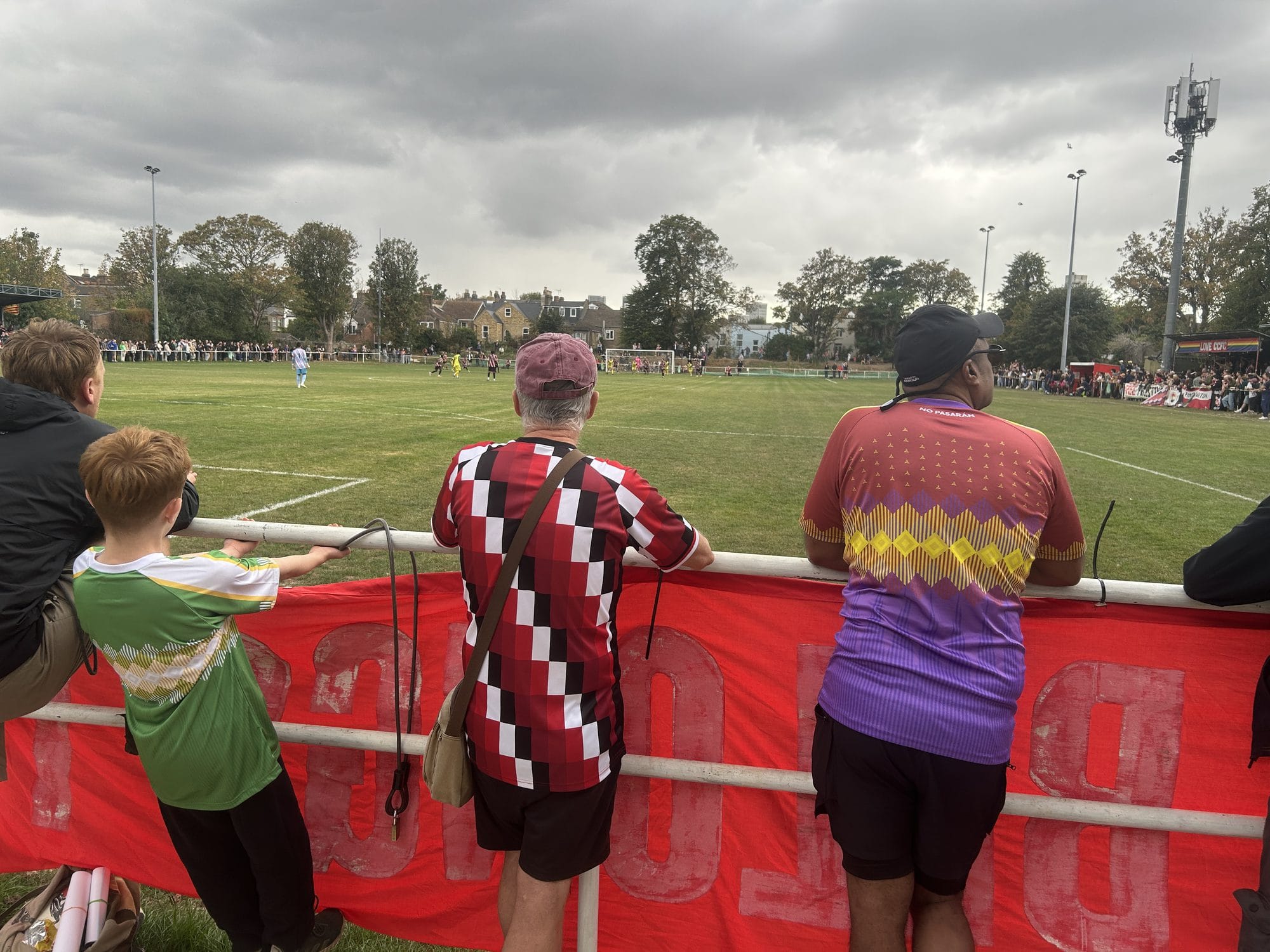 Three men and a boy leaning on the pitchside rail, side by side, watching the game