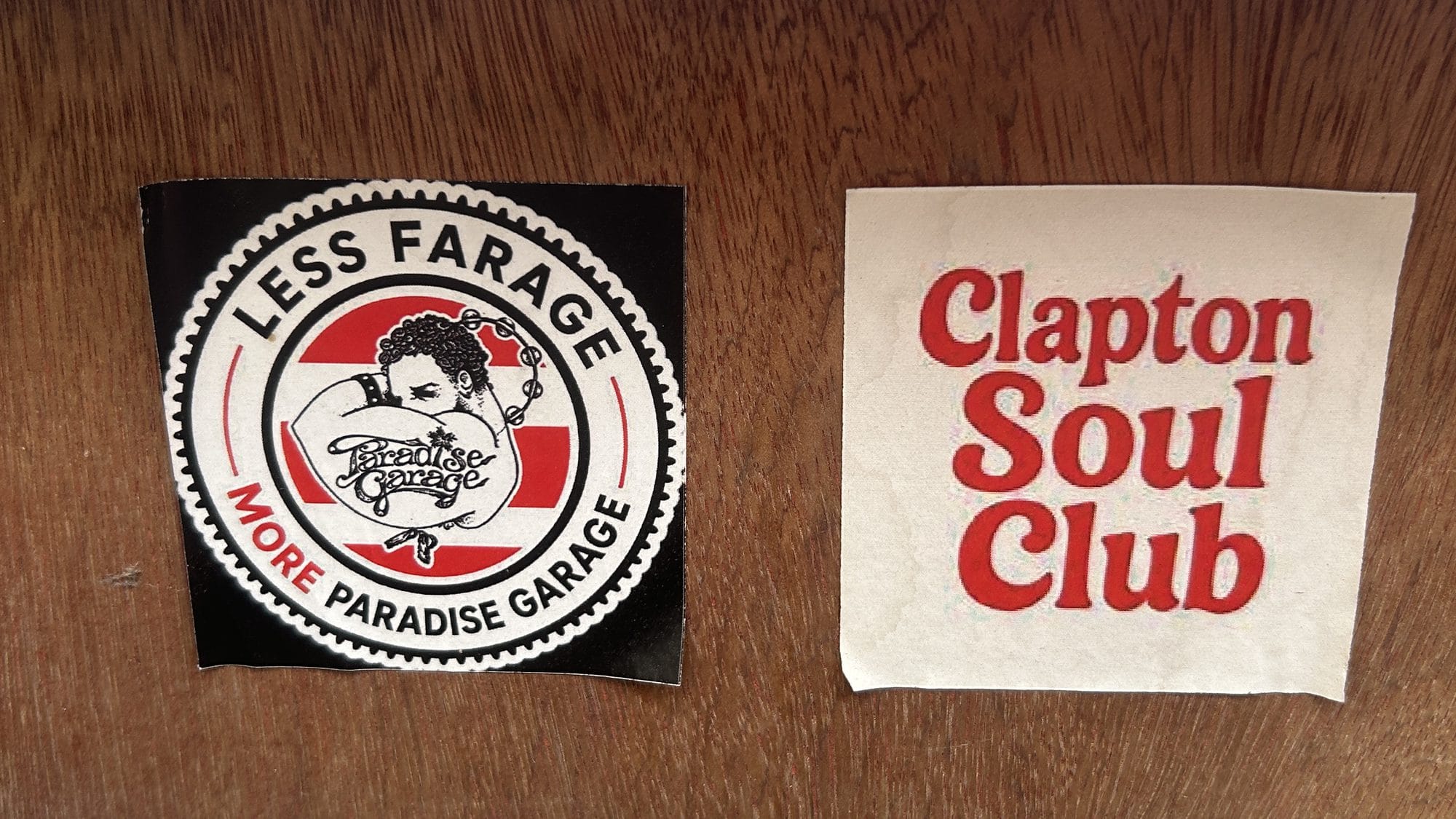 Two stickers side by side on a wooden board: "Less Farage, More Paradise Garage" and "Clapton Soul Club"