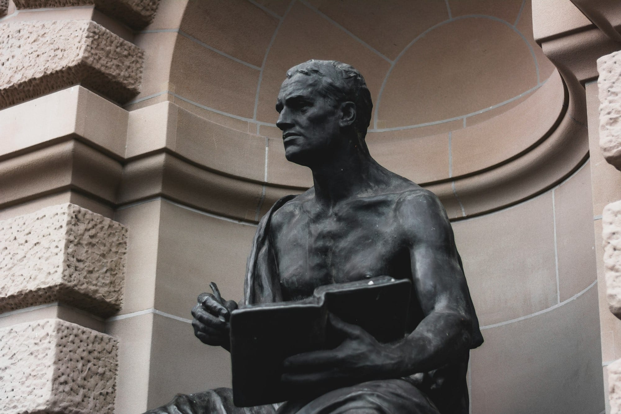 a statue of a man holding a book in front of a building