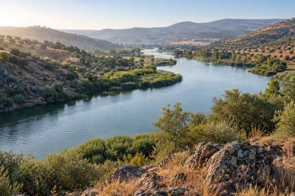 Rio entre colinas secas e vegetação ribeirinha no sul da Península Ibérica, em paisagem ilustrativa inspirada na região do Guadiana.