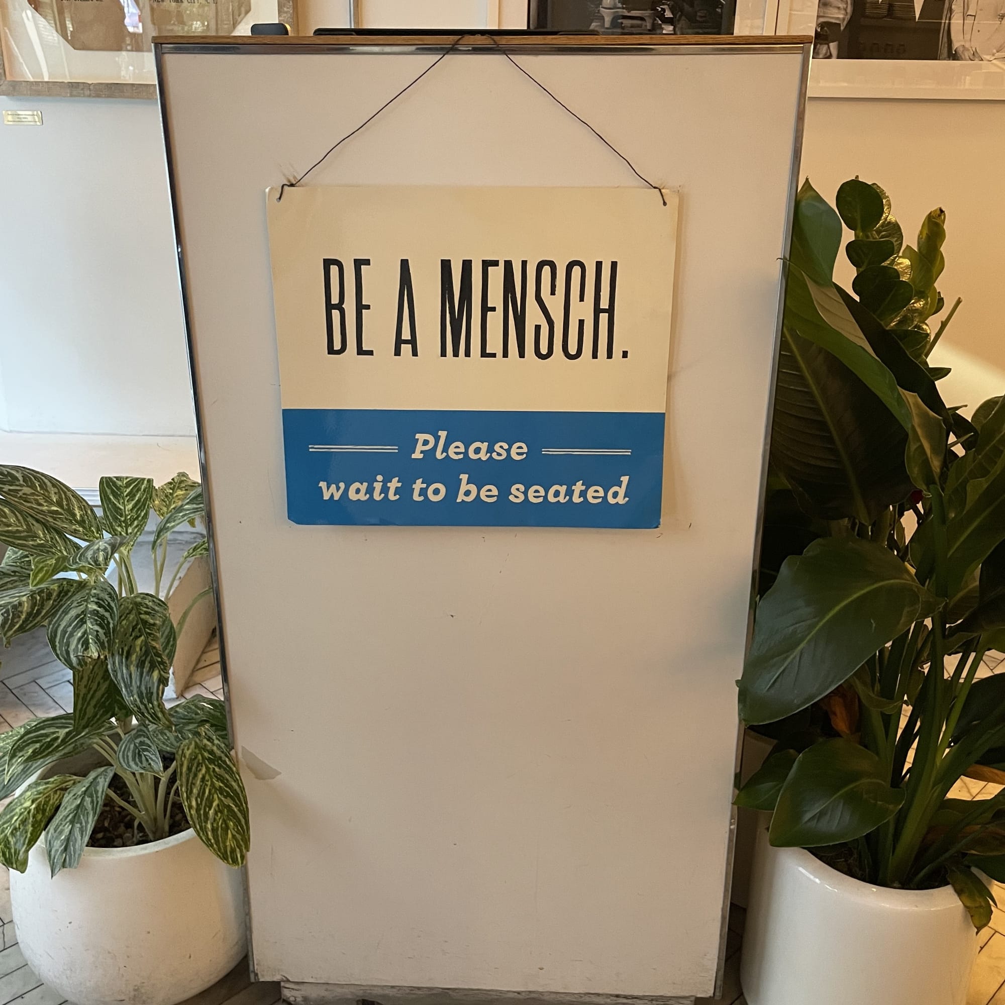 Russ & Daughters Cafe host stand with a sign reading "Be a Mensch, please wait to be seated"
