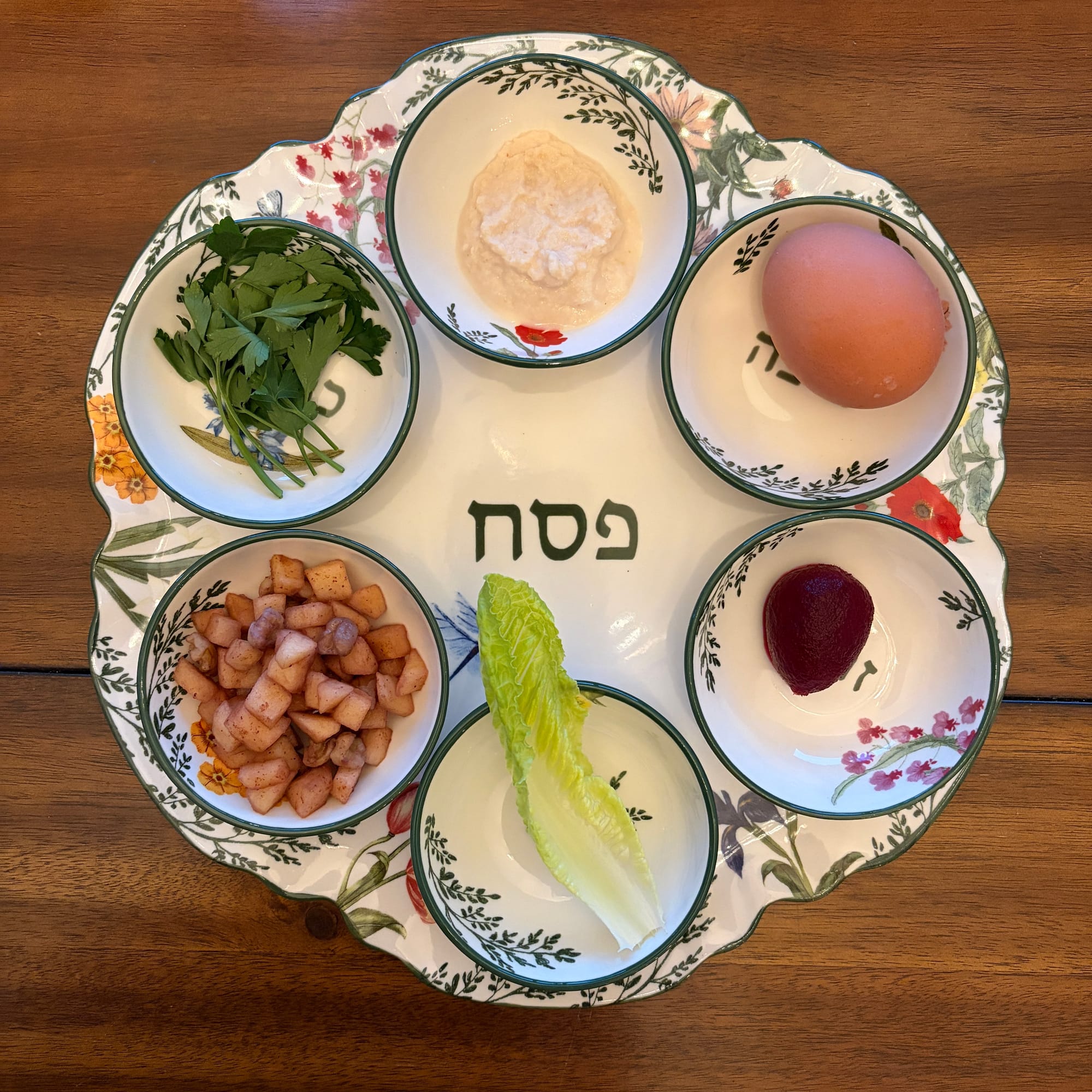 White seder plate with painted floral decorations, filled with ritual foods for Passover