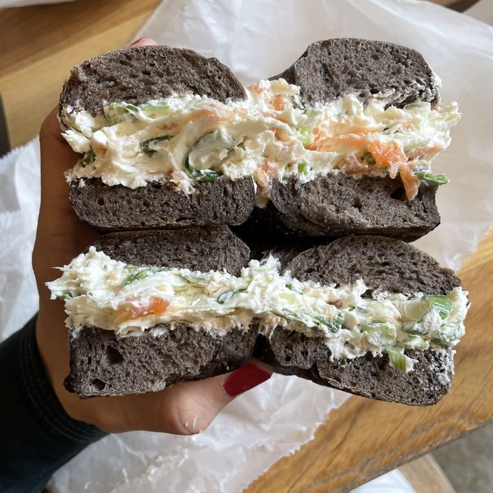 Stacy's hand holding two halves of a pumpernickle bagel with lox and scallion cream cheese