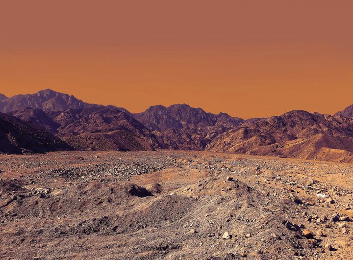 Brown rocky desert with jagged mountains in the distance and an orange sky