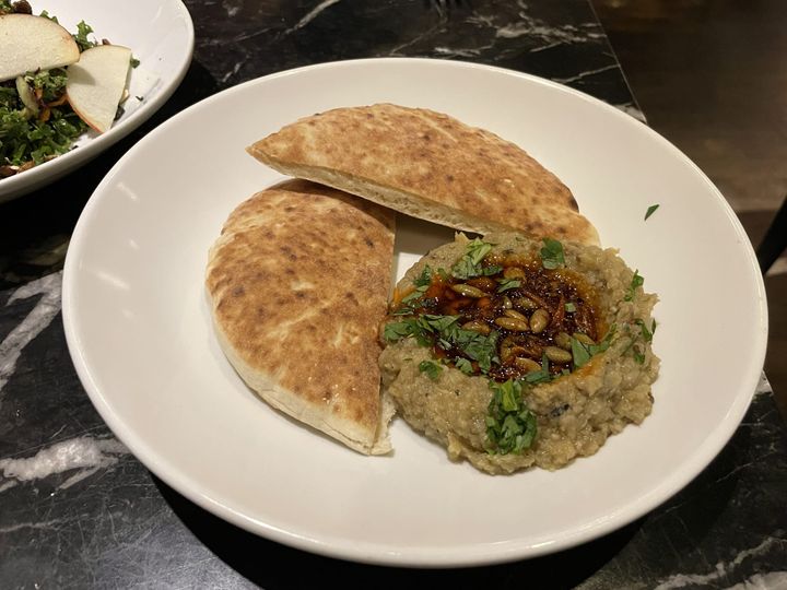 Plate with two pita halves and eggplant dip garnished with seeds, chili oil, and cilantro