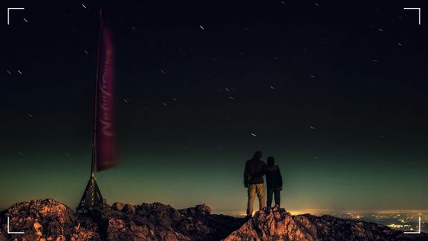 Two People standing on a mountaintop under the starry night.