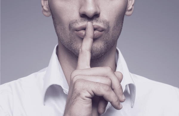 Mann in weißem Hemd legt den Zeigefinger auf die Lippen – Geste des Schweigens, Duotone in Tintenlila. Titelbild des Whitepapers „Die Kosten des Schweigens".