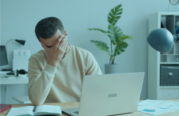Erschöpfte Führungskraft am Schreibtisch, Hand vor dem Gesicht, vor Laptop und Notizen