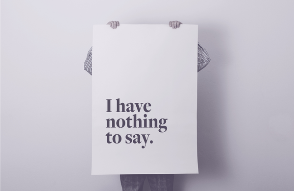 Person verbirgt sich hinter einem großen Plakat mit der Aufschrift „I have nothing to say"; nur Hände und Beine sind sichtbar.