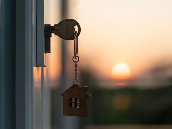 A key in a door lock with a house-shaped keychain, sunset softly blurred in the background, symbolizing home and tranquility.