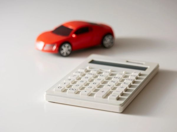 A white calculator with large buttons next to a bright red toy car, both placed on a clean, white surface.