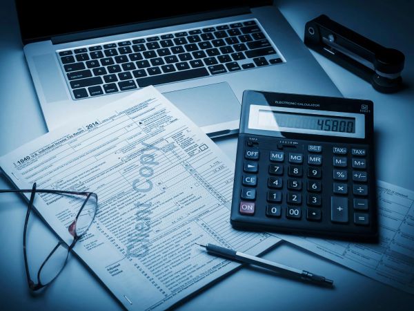 A laptop on a glass table displaying financial charts and data dashboards, including bar graphs, line charts, and key performance metrics.