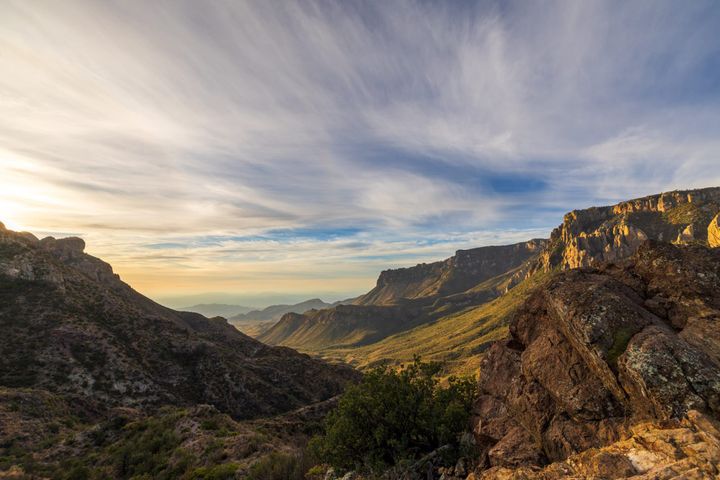 Green meadows slope down a valley while a cloudy sky creates a dramatic effect shortly after sunrise. Big Bend National Park.