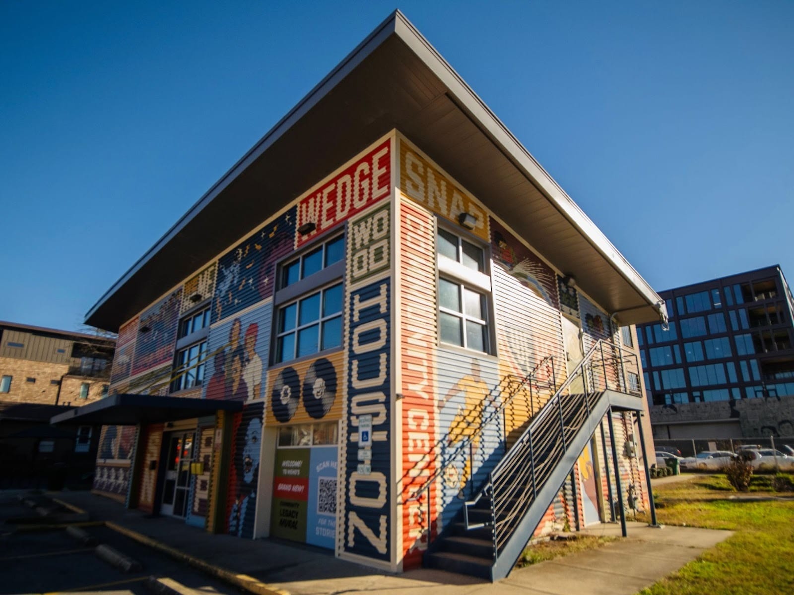 Close-up view of a brick building at 1224 Martin Street, photographed from below to emphasize scale, with a mural reading “Wedgewood-Houston” and “SNAP Community Center.”