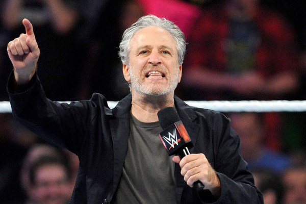 Jon Stewart pointing with microphone in hand in WWE ring