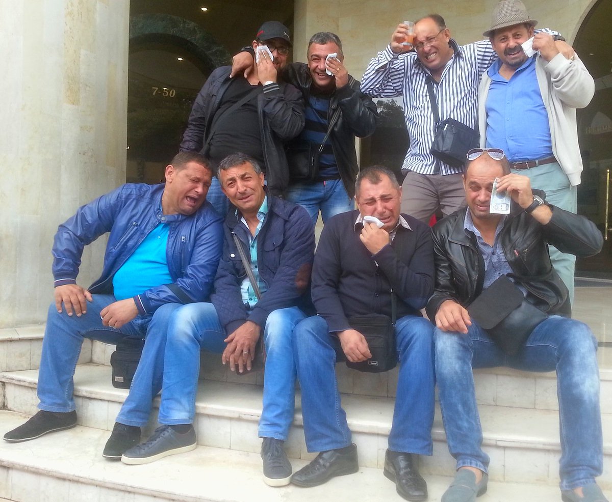 Eight bandmates jokingly crying while sitting on steps