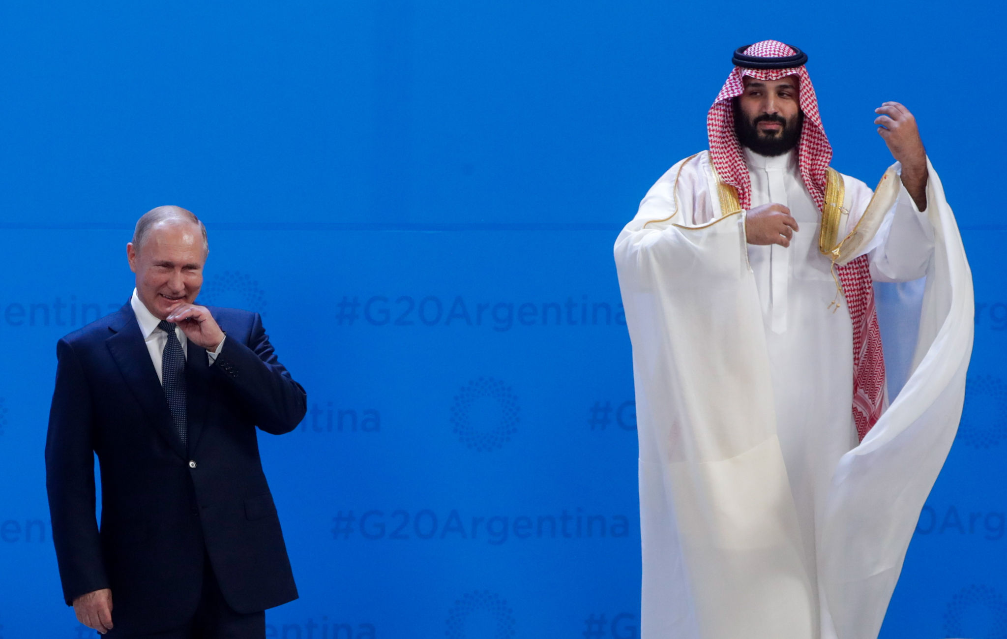 Vladimir Putin and Mohammed bin Salman at the G20 Argentina, Putin giggling while bin Salman is looking at him, the latter with his hands in the air looking as if he's playing an instrument