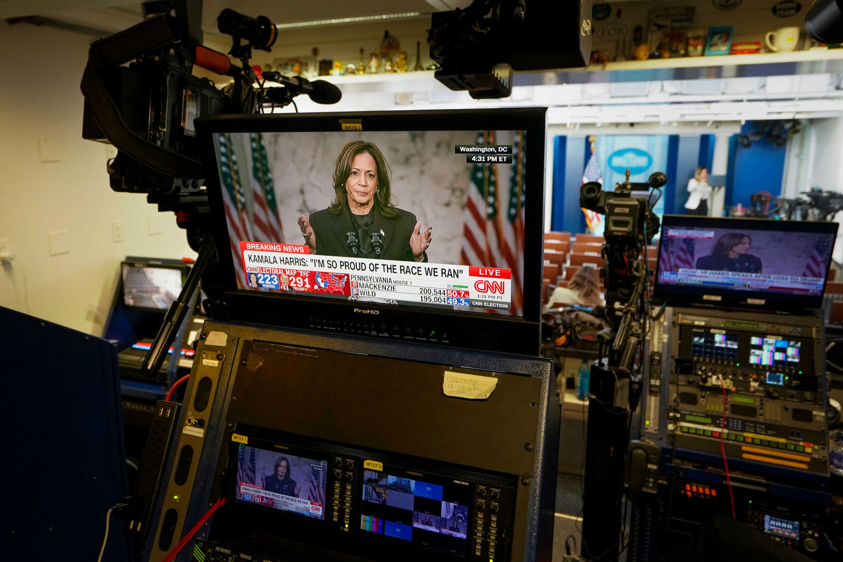 Kamala Harris depicted on video screens giving her concession speech, in the White House Press Briefing Room
