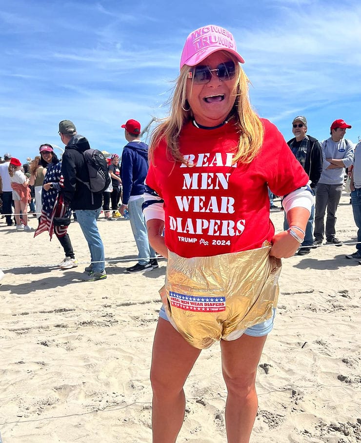 A woman wearing a "Real Men Wear Diapers" t-shirt while holding a golden "Real Men Wear Diapers" diaper against her shorts