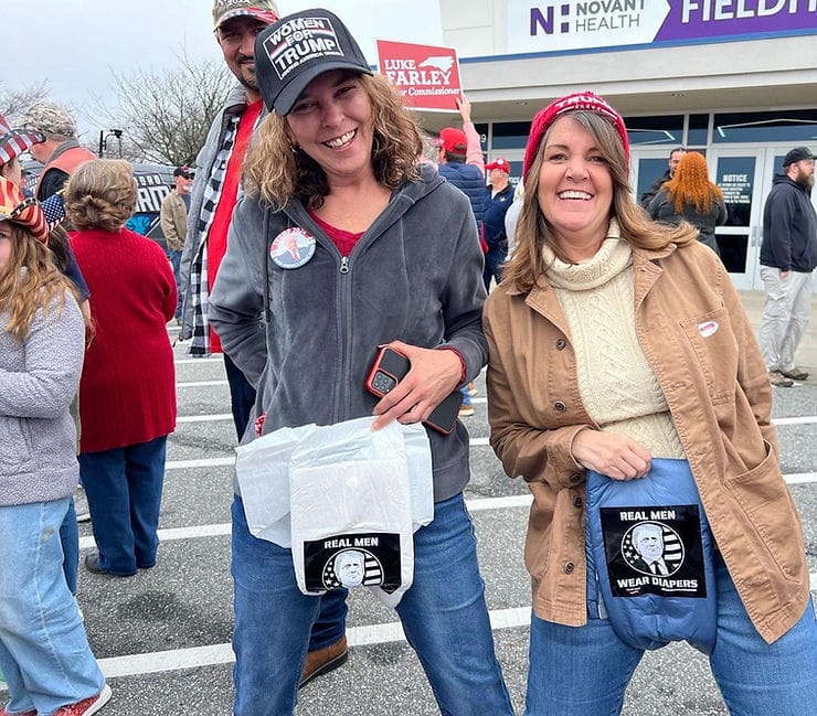 Two smiling women holding "Real Men Wear Diapers" diapers up against their pants