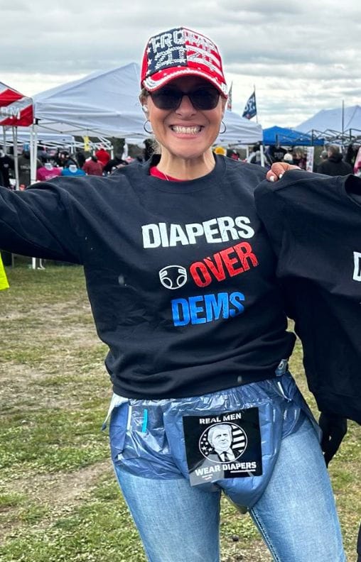 A woman wearing a "Real Men Wear Diapers" diaper over her pants, as well as a "Diapers over Dems" sweater