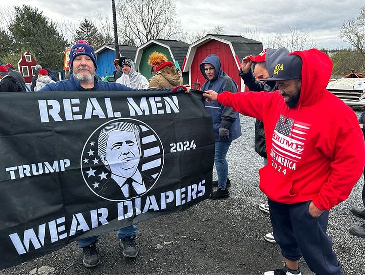 A man holding up a "Real Men Wear Diapers" banner
