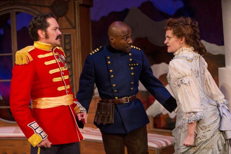 A man in a 19th century military uniform stands between another man in uniform and a woman as they argue.