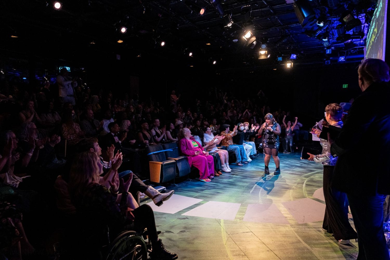 In a theatre, audiences clap and cheer for people on stage accepting awards.